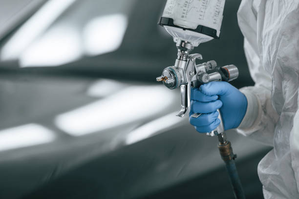 Focused close up view. Man is holding spray gun for painting a car